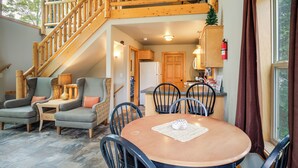 Un intérieur chaleureux avec un escalier en bois, un coin repas doté d’une table ronde et une cuisine visible au fond.