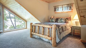 Une chambre avec un plafond en pente, une grande fenêtre, un cadre de lit en bois et une lampe de chevet.