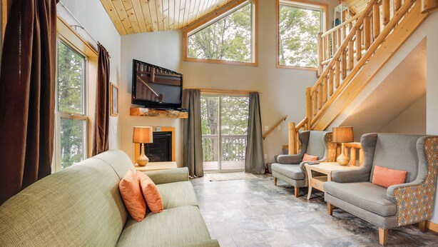 Un salon spacieux avec un haut plafond, un escalier en bois et de grandes fenêtres.