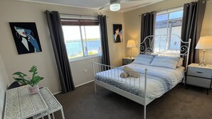 Une chambre à coucher comprenant un lit, des tables de chevet, un bureau, une chaise, un ventilateur de plafond et une fenêtre avec des rideaux.