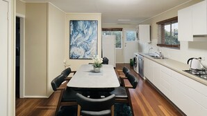 Une cuisine moderne avec des meubles blancs, une table à manger avec des chaises, un tapis noir et un grand tableau abstrait accroché au mur.