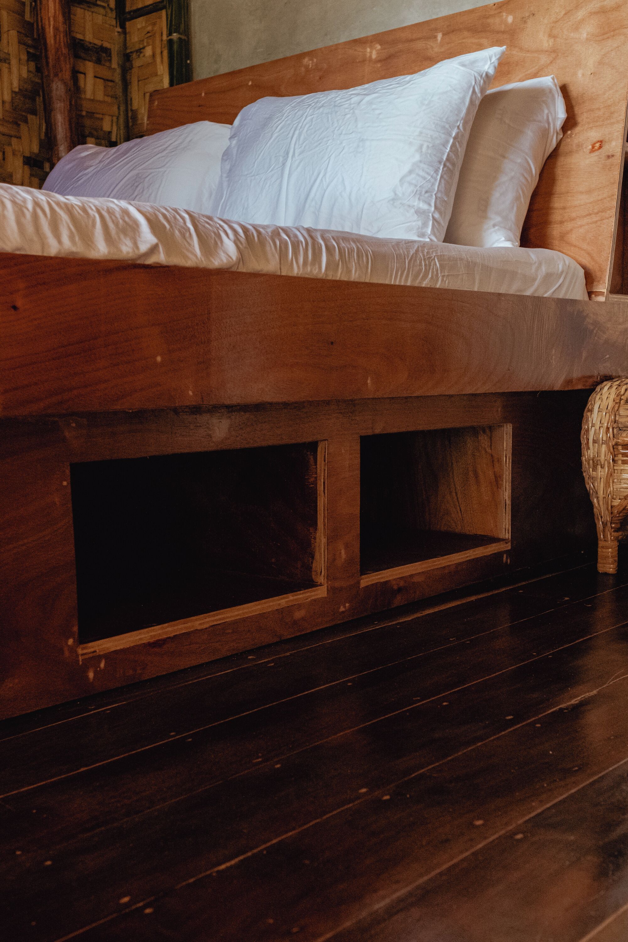 A wooden bed with white bedding, a woven basket, and a dark wooden floor.