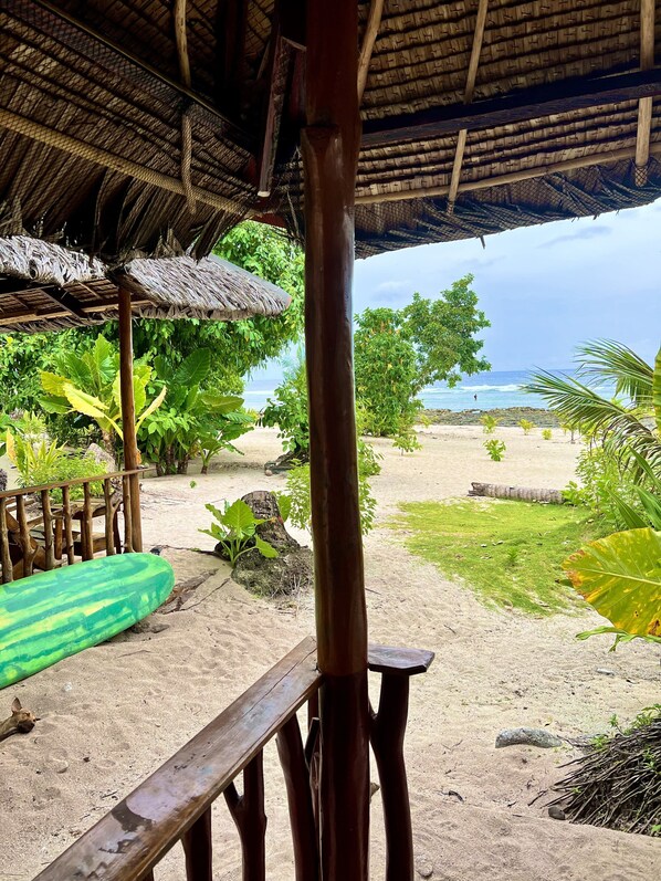 A beach view with a thatched roof structure, wooden benches, and a green surfboard. - Marahuyo Siargao (General Luna)