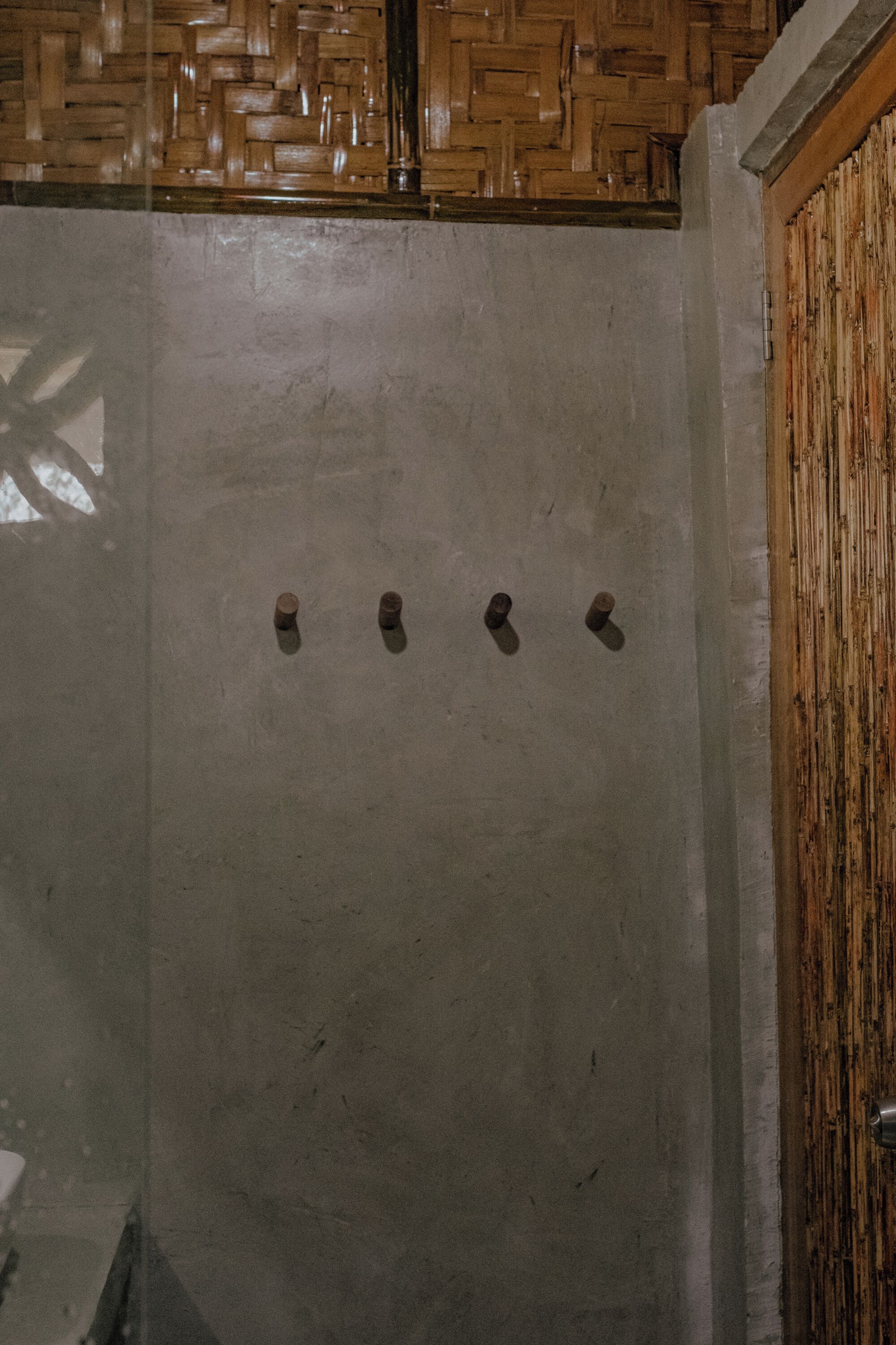 A concrete shower enclosure with a wooden door and a woven ceiling.