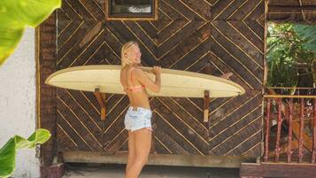 Una persona sosteniendo una tabla de surf frente a una estructura de madera con un diseño en zigzag.