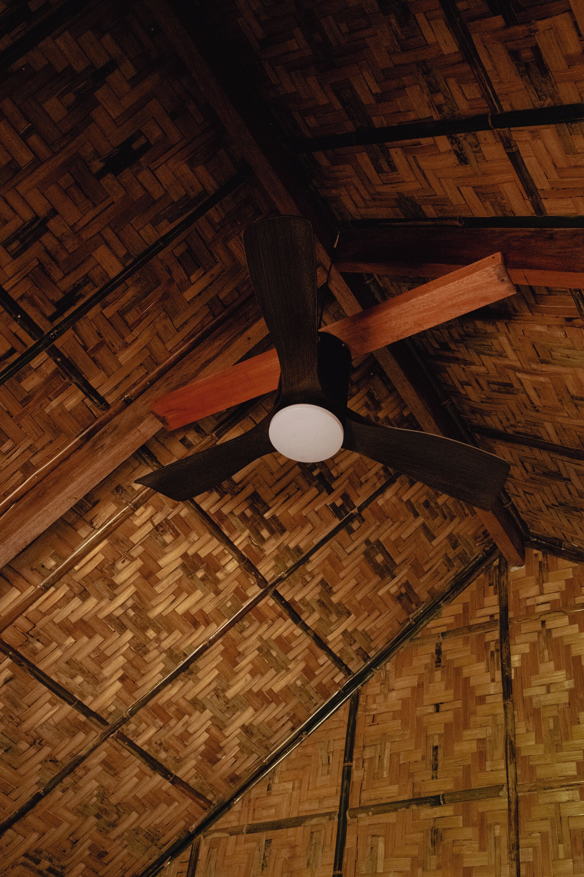 A ceiling fan with wooden blades and a central light fixture in a room with a herringbone-patterned wooden floor.