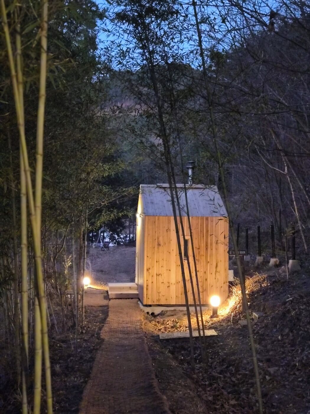 A wooden cabin with a pathway leading to it, surrounded by trees.