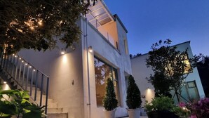 Ein modernes, zweistöckiges Haus mit Glastür, Topfpflanzen und gut beleuchteter Fassade.