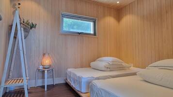 A bedroom with wooden walls, a window, a ladder, and a bedside table with a lamp.