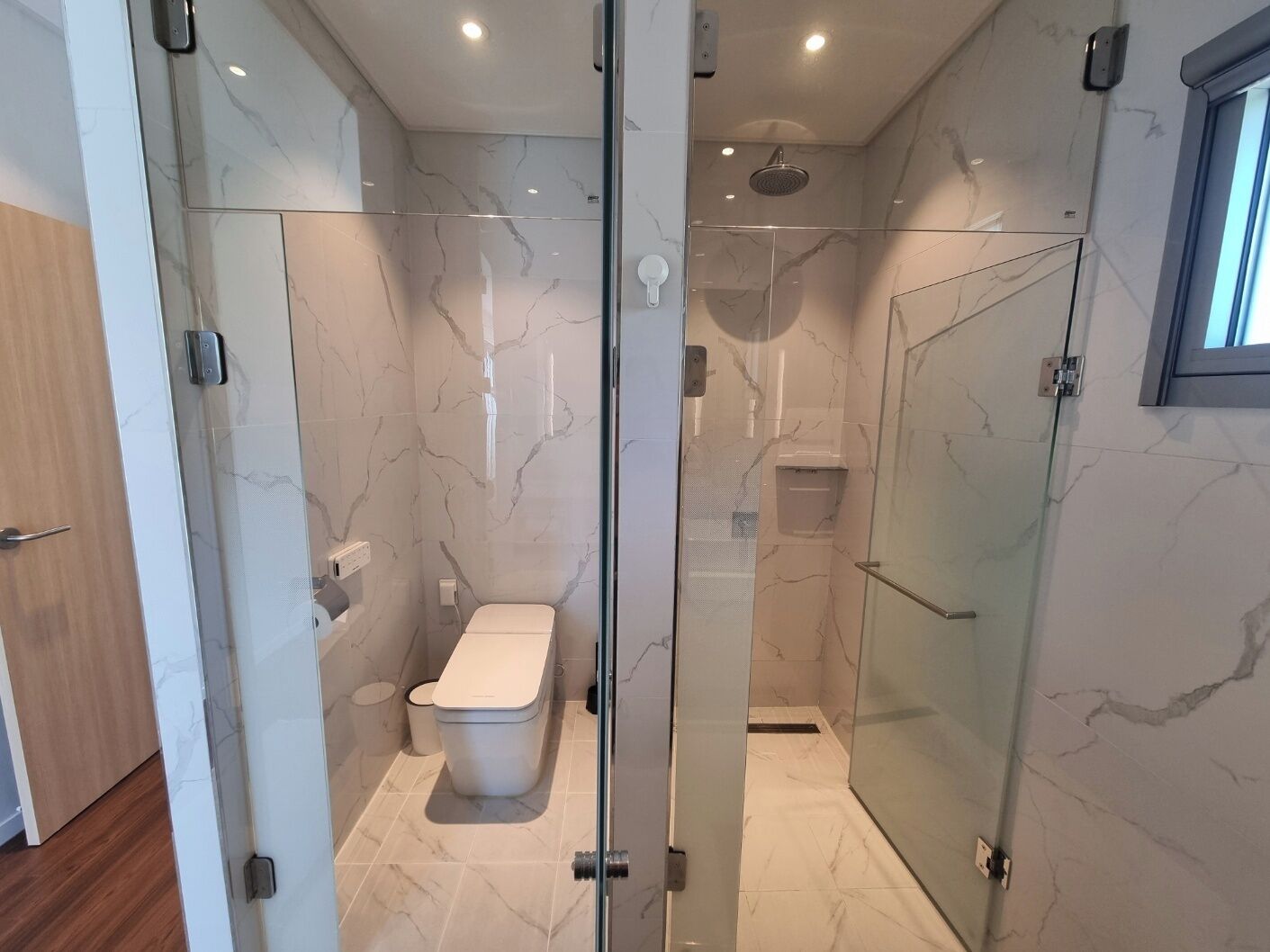 Un baño moderno con ducha de vidrio, inodoro y suelo de mármol.