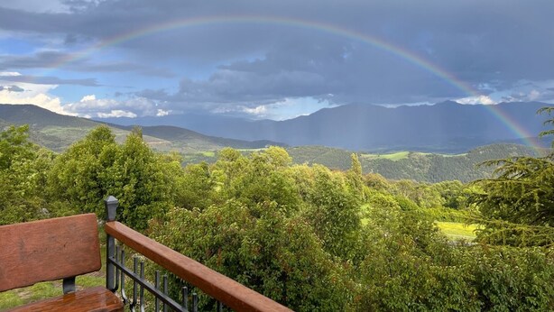 A bench overlooking a lush landscape with a rainbow arching across the sky.