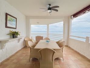 A dining area with a table and chairs, a ceiling fan, a potted plant, and a view of the sea.