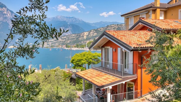 A coastal house with a balcony, a view of the sea, and mountains in the background. - Villa Il Paradiso Di Gabri: Lake-view Villa With Garden (Nago-Torbole)