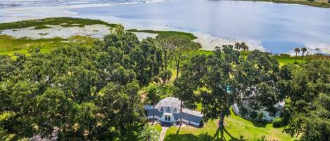 A house surrounded by dense forest and a large body of water.