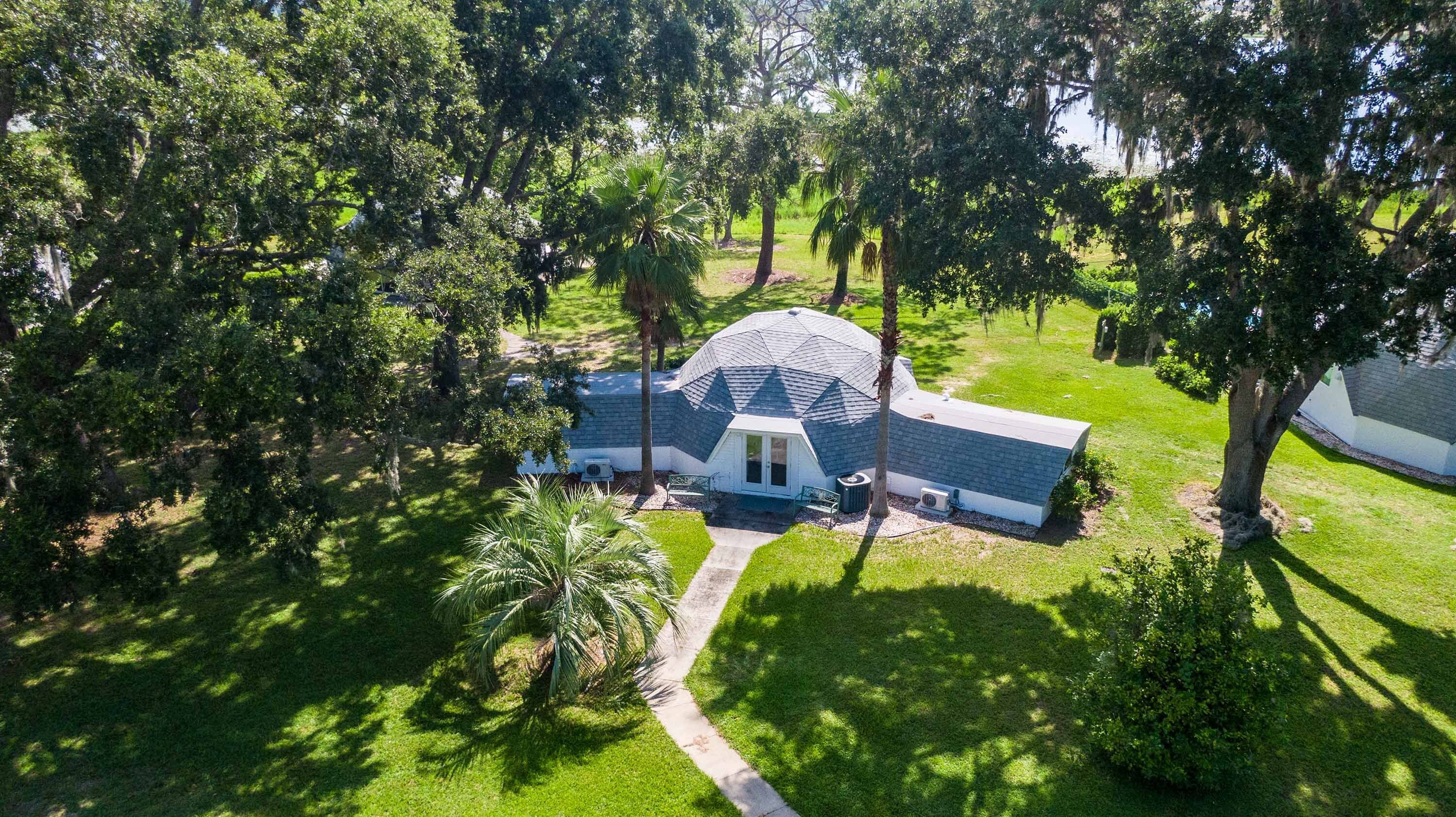 An aerial view of a house with a sloped roof, surrounded by lush greenery and trees.