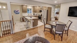 A modern kitchen with wooden cabinets, a central island, and a dining area with a table and chairs.