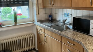 Una cocina con armarios de madera, encimera de granito, microondas integrado y una ventana con persianas.