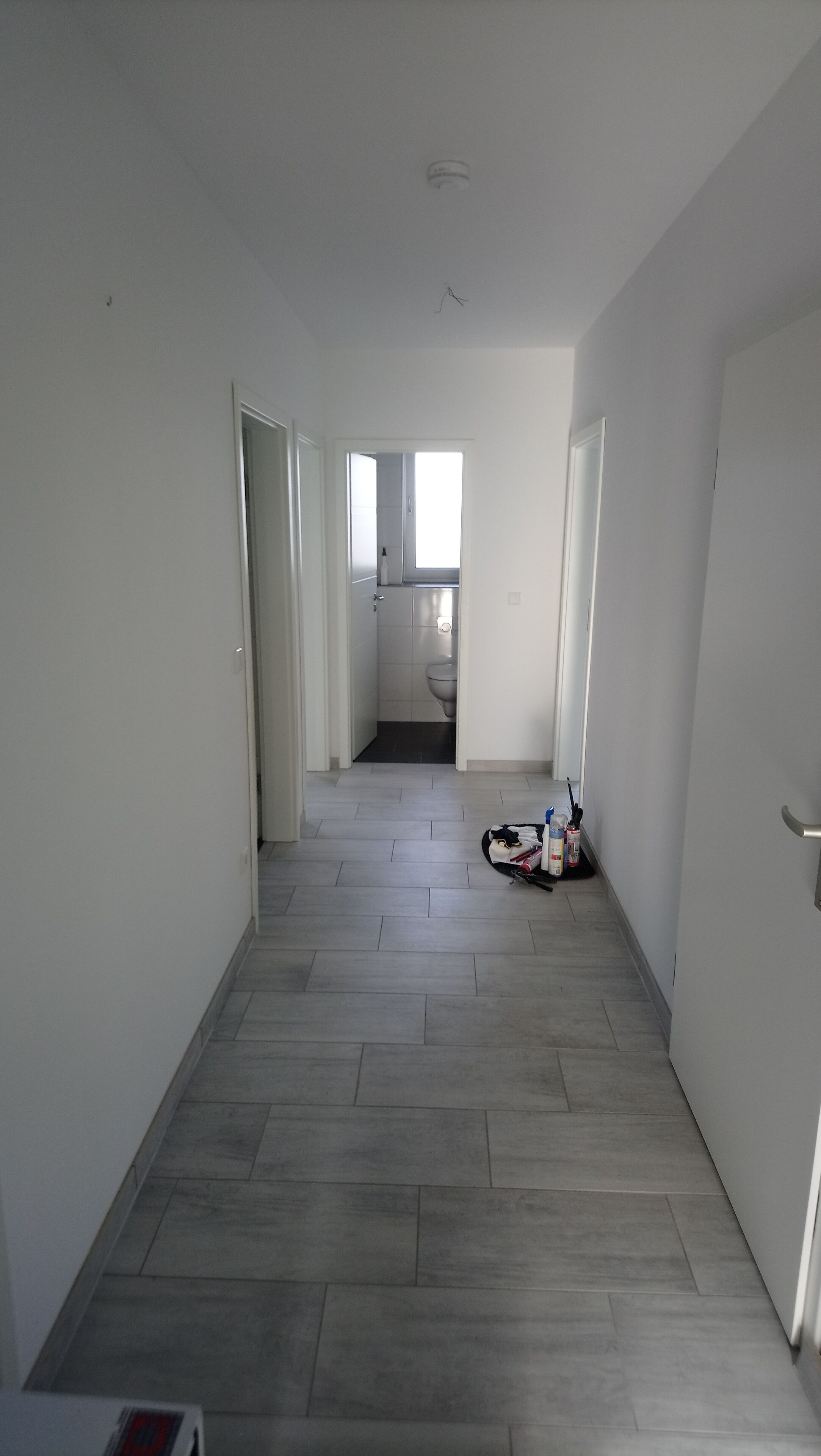 A hallway with grey tiled flooring, white walls, and doors leading to other rooms.