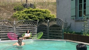 Ein Schwimmbecken mit Holzzaun, ein Haus im Hintergrund und ein klarer Himmel.