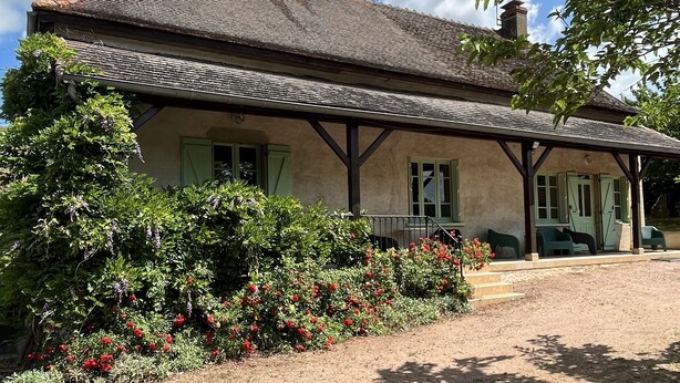 Ein rustikales Haus mit Ziegeldach, grünen Fensterläden und einer Veranda.