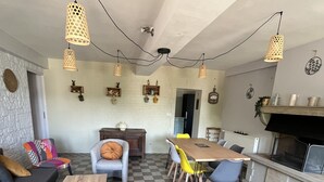 Ein Wohnzimmer mit Schachbrettmuster-Boden, einer Couch, einem Couchtisch, einem Esstisch mit Stühlen und hängenden Pendelleuchten.