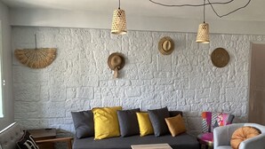 Ein modernes Wohnzimmer mit einer Wand im Steinoptik, einem grauen Sofa mit gelb-grauen Kissen, einem Holztisch und einem grauen Sessel.