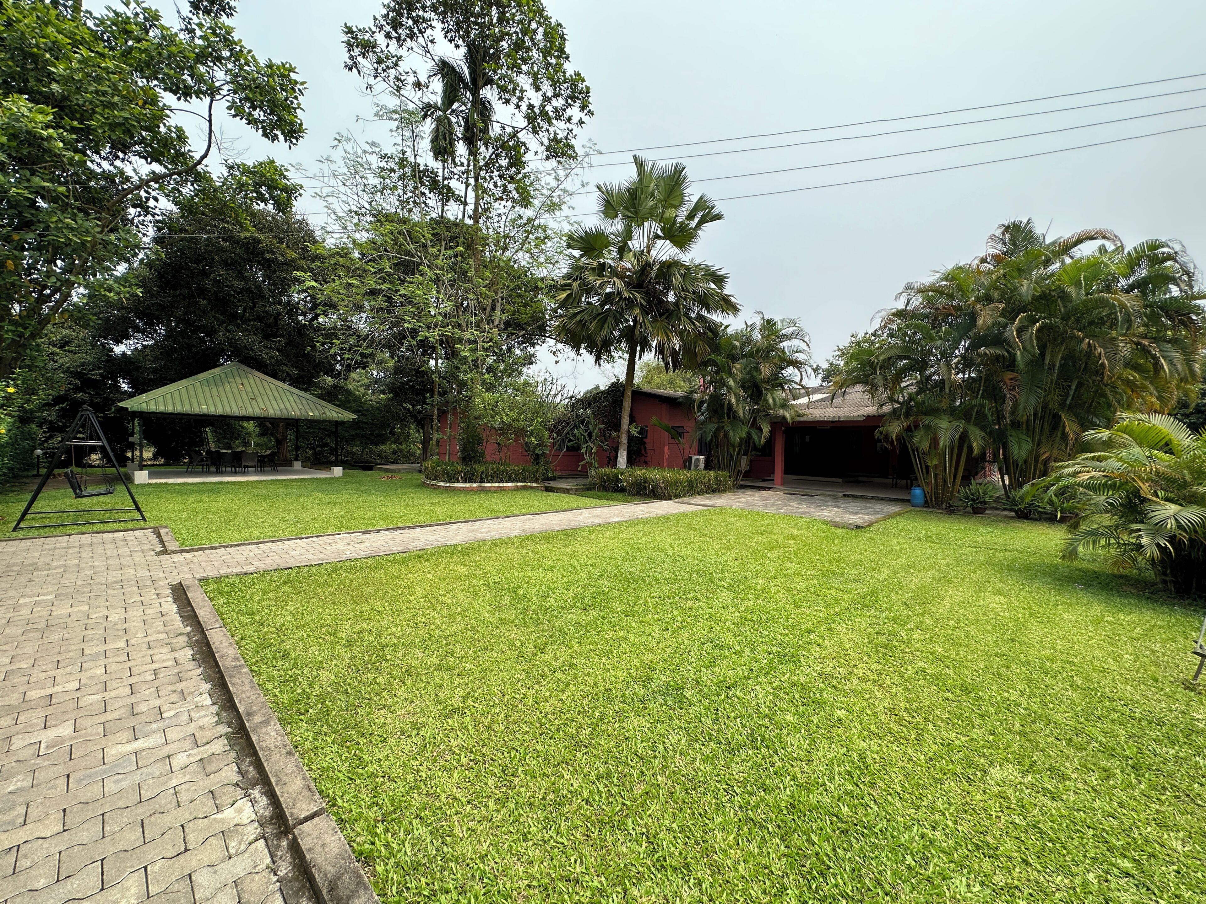 A well-maintained lawn with a swing set, a covered pavilion, and a building with a red exterior.