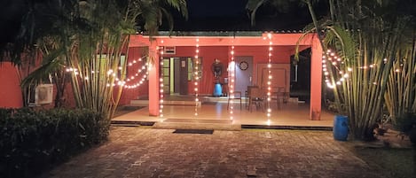 A covered outdoor area with string lights, palm trees, and a brick pathway.