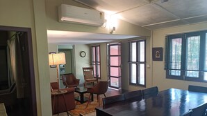 A dining area with a long table and chairs, a wall-mounted air conditioner, and a clock on the wall.