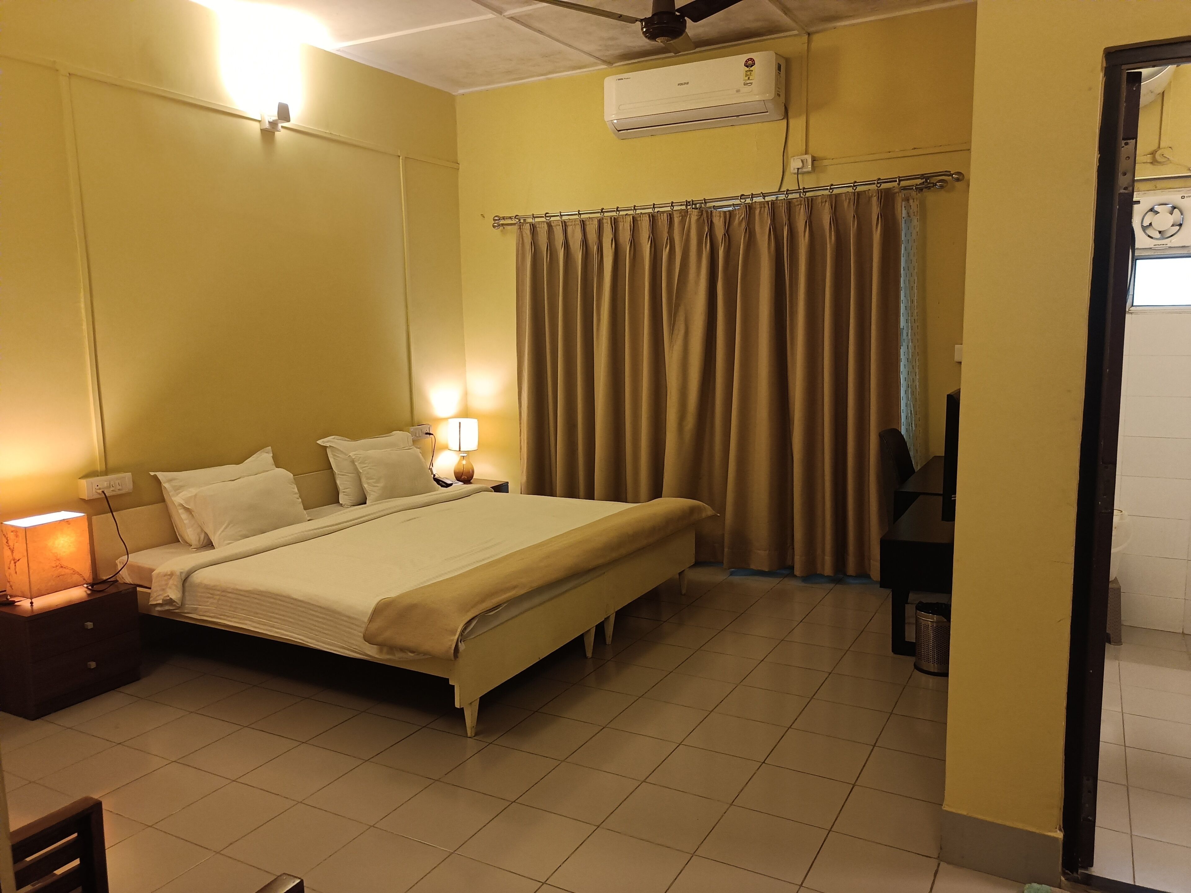 Une chambre d’hôtel équipée d’un lit, d’une lampe de chevet, d’un climatiseur, de rideaux et d’un sol carrelé.