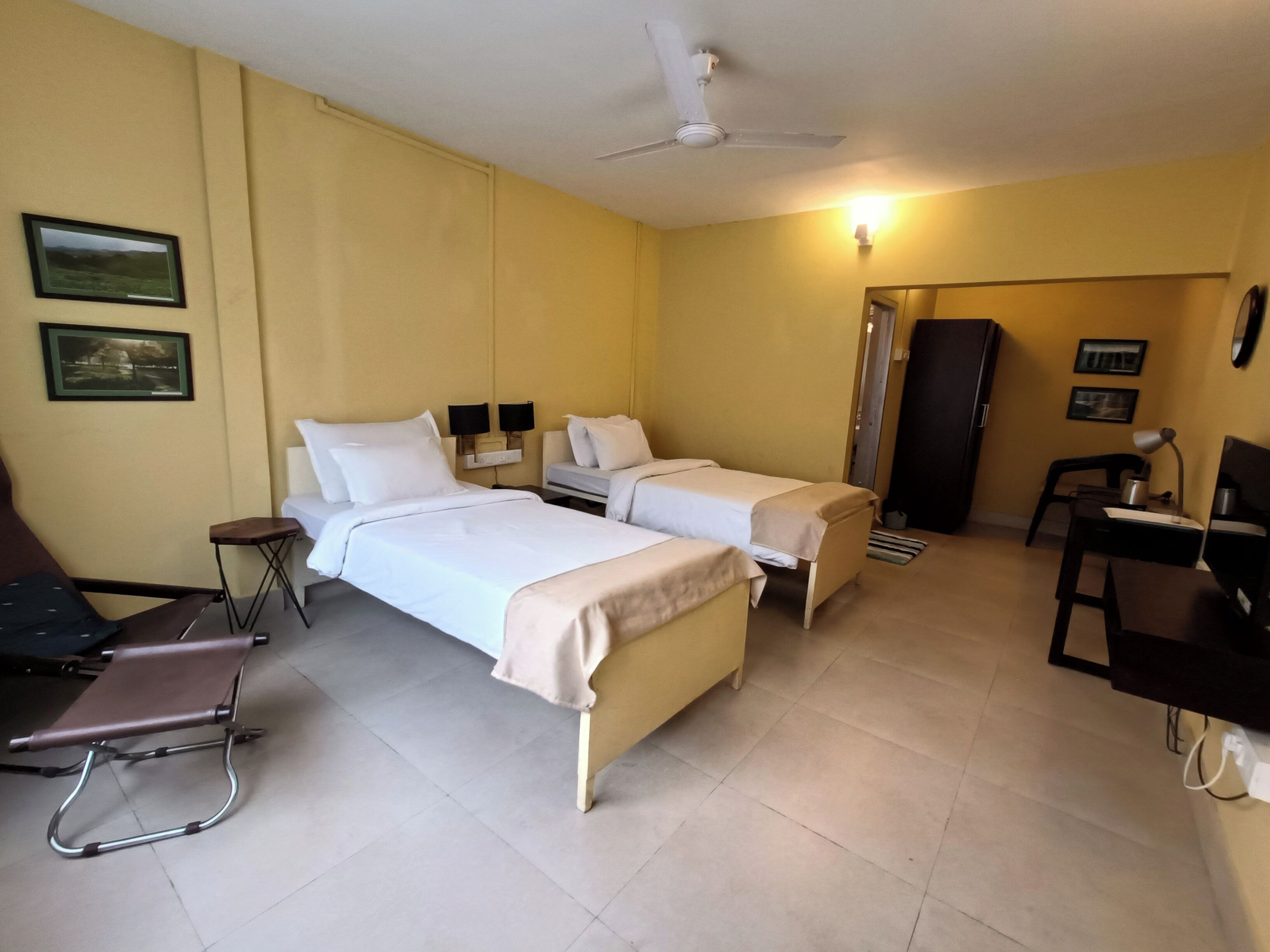 A hotel room with two beds, a desk, a chair, a ceiling fan, and a door.