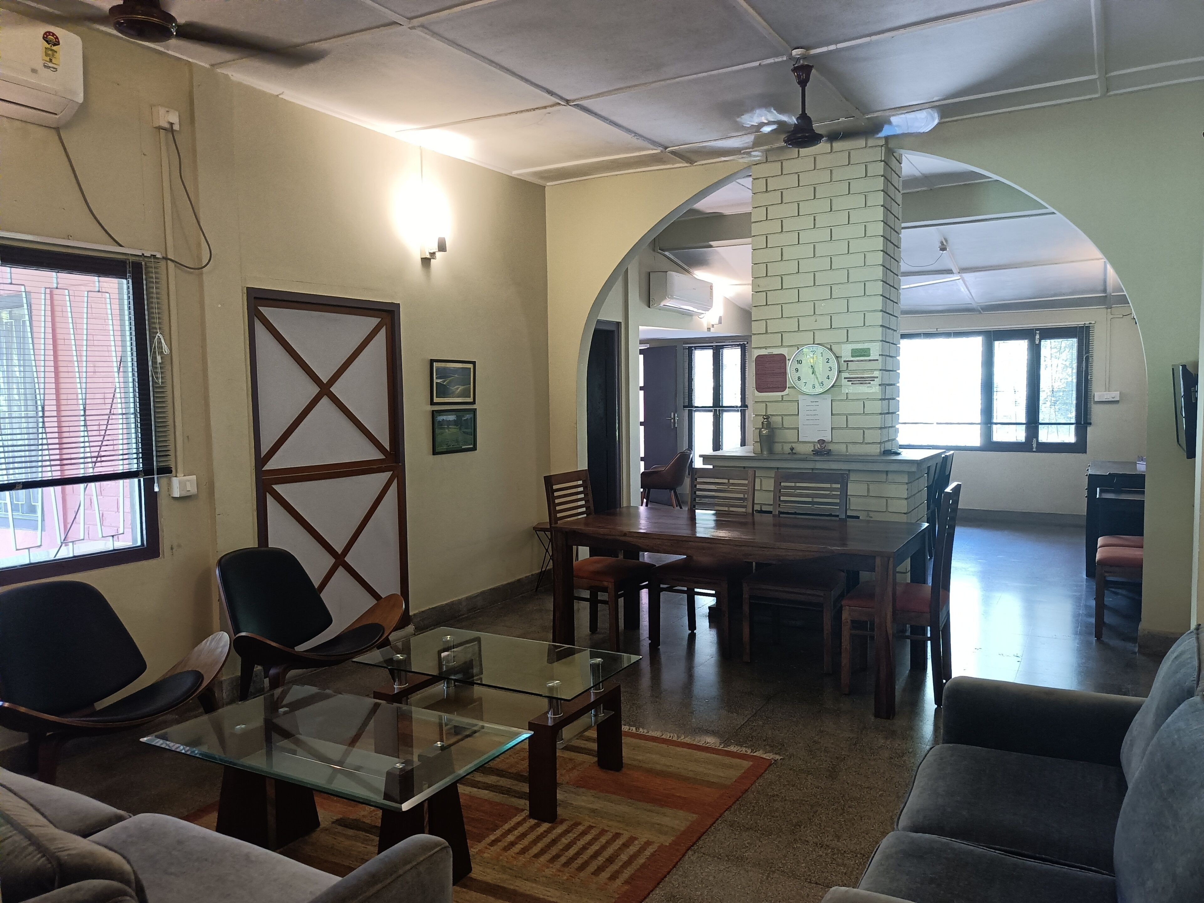 A spacious living area with a glass coffee table, comfortable seating, a brick accent wall, and a view through an archway.