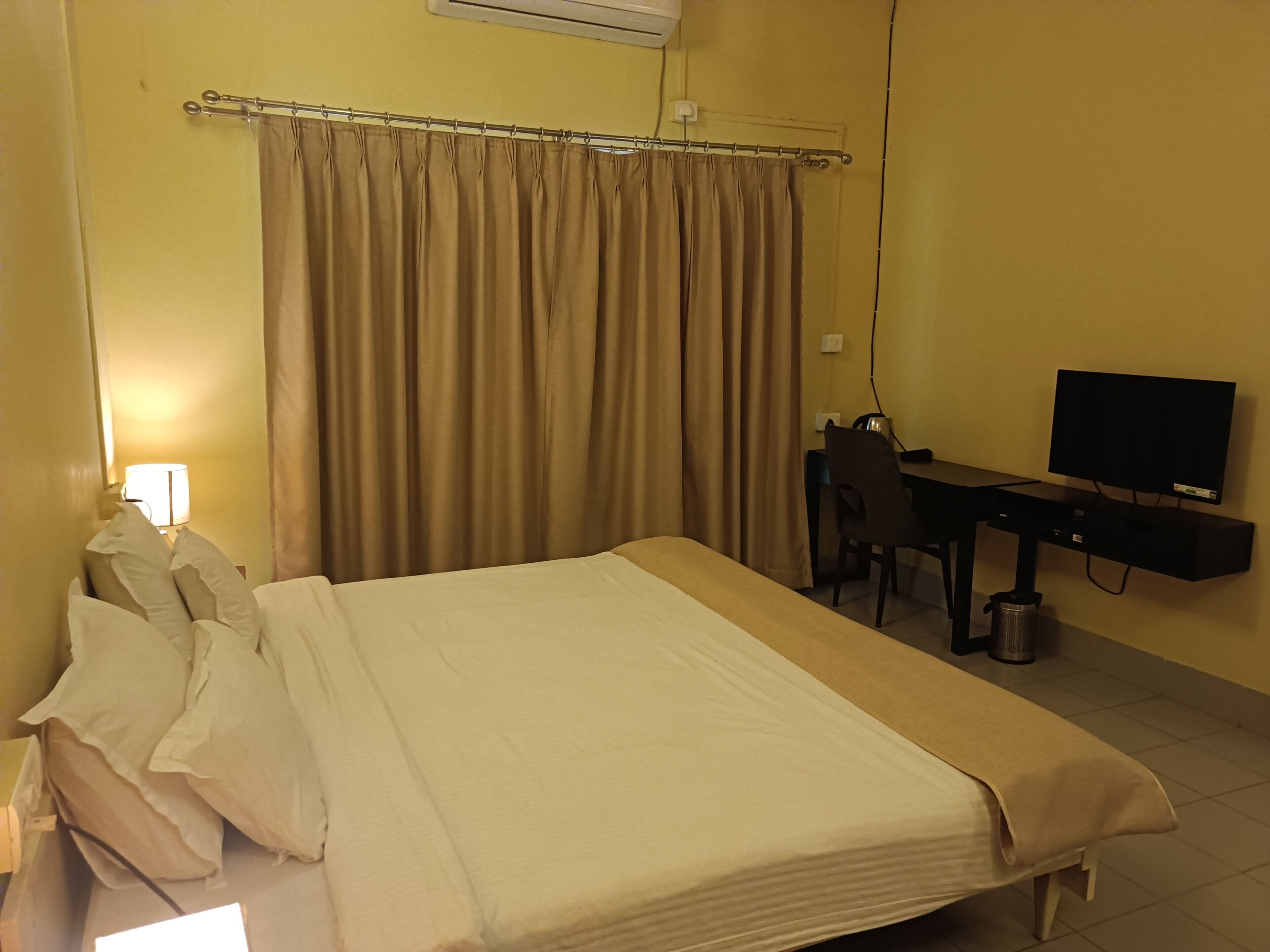 A hotel room with a bed, a desk, a chair, a television, and a lamp.