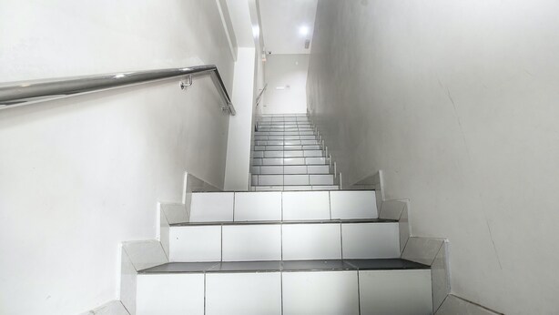 Uma escadaria moderna e estreita, com corrimãos de metal e degraus brancos que conduzem para cima.