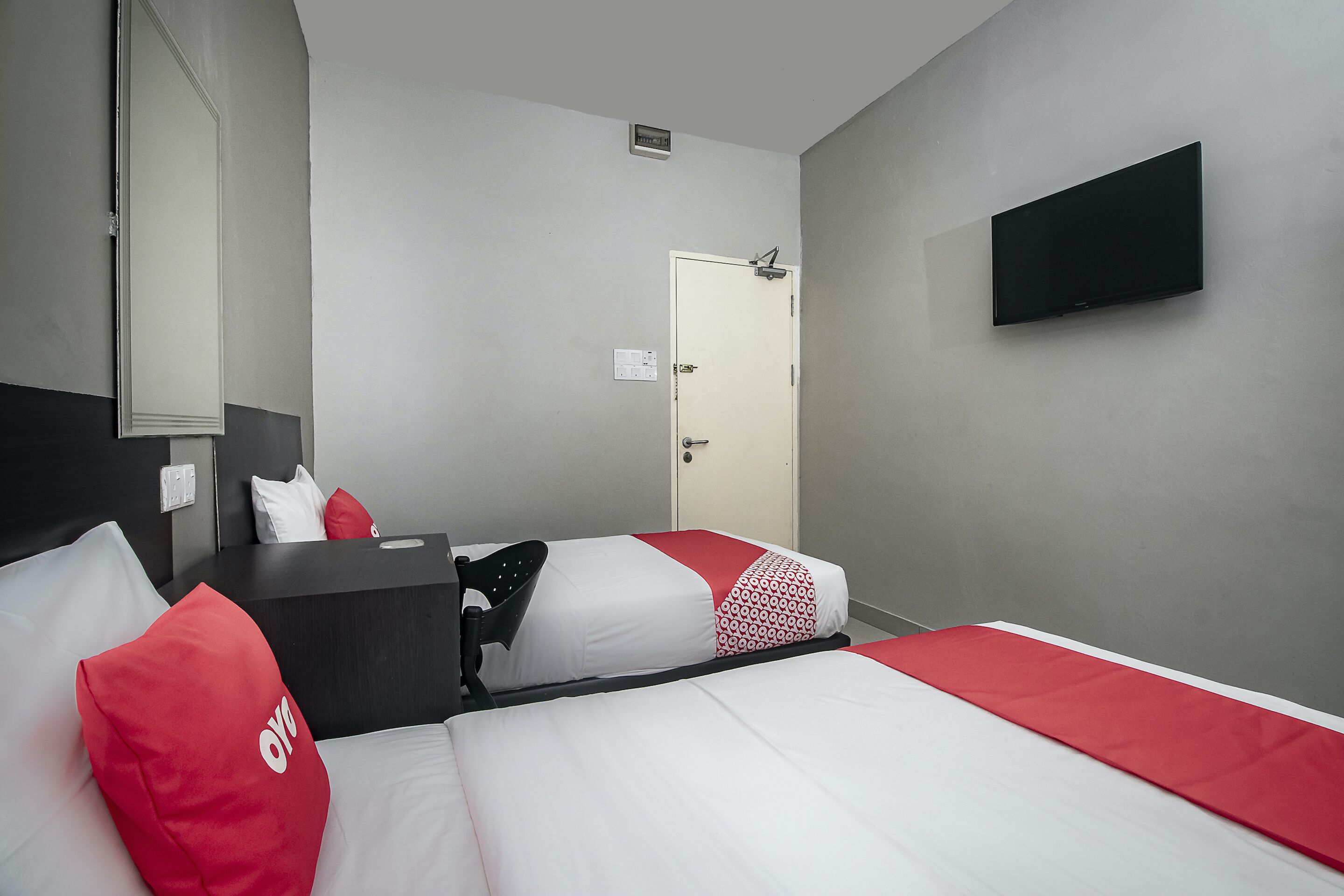 A hotel room with two beds, a TV mounted on the wall, a door, and a mirror.