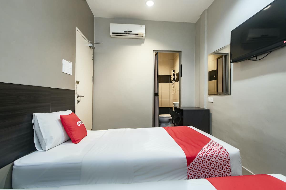 A hotel room with a bed, a TV mounted on the wall, and an air conditioning unit.