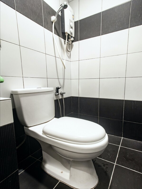 Un inodoro blanco con un cabezal de ducha montado encima, frente a una pared de azulejos con diseño de blanco y negro.