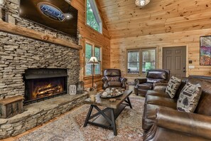 L’intérieur d’un chalet en rondins, avec une cheminée en pierre, des meubles en cuir et une enseigne indiquant « Blue Sky Cabin Rentals ».