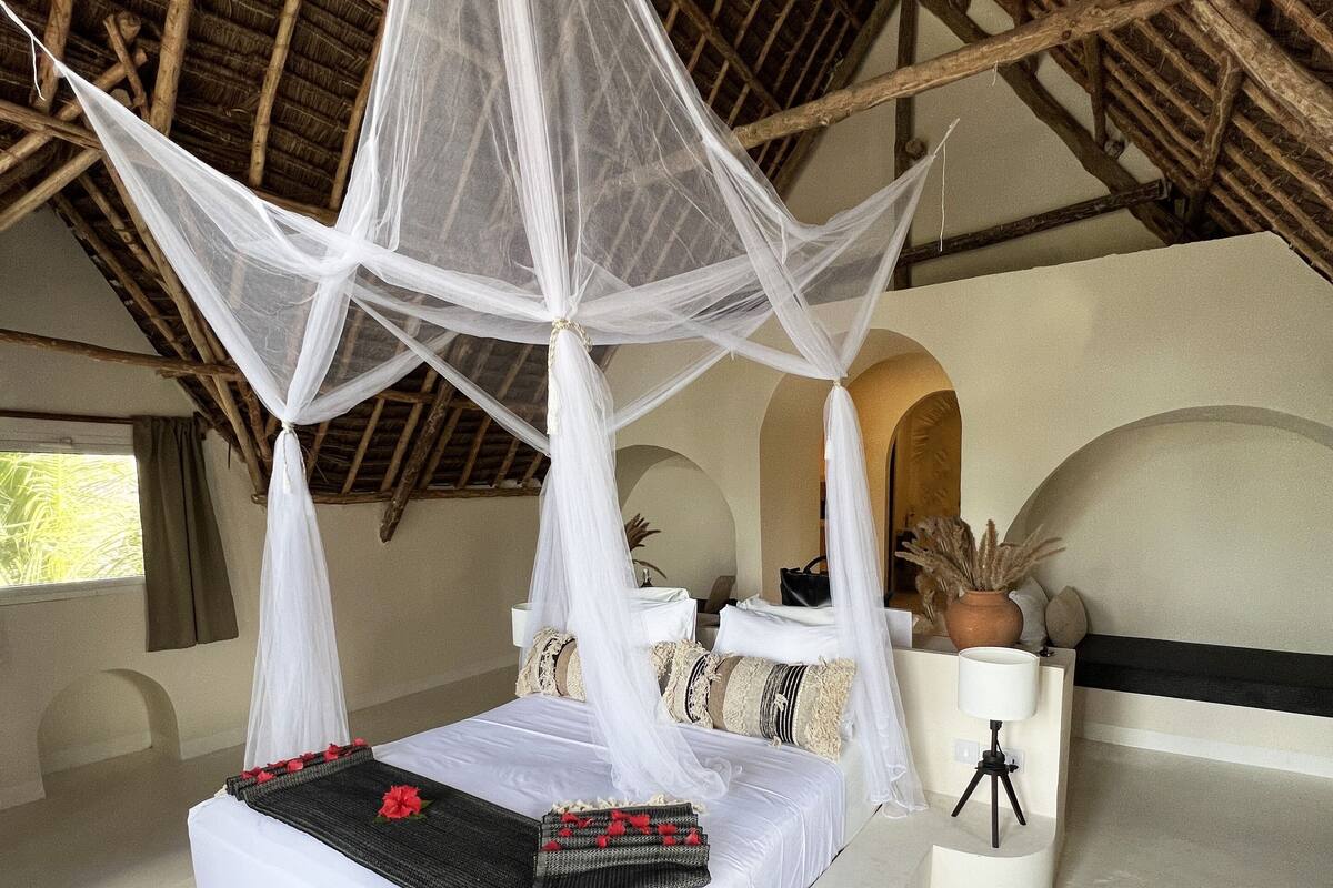 A bed with a canopy, a potted plant, and a tripod lamp.