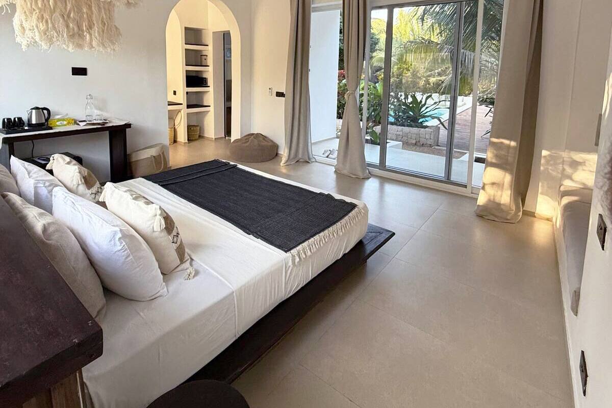 A modern bedroom with a large bed, a desk, and a view of the outdoors.