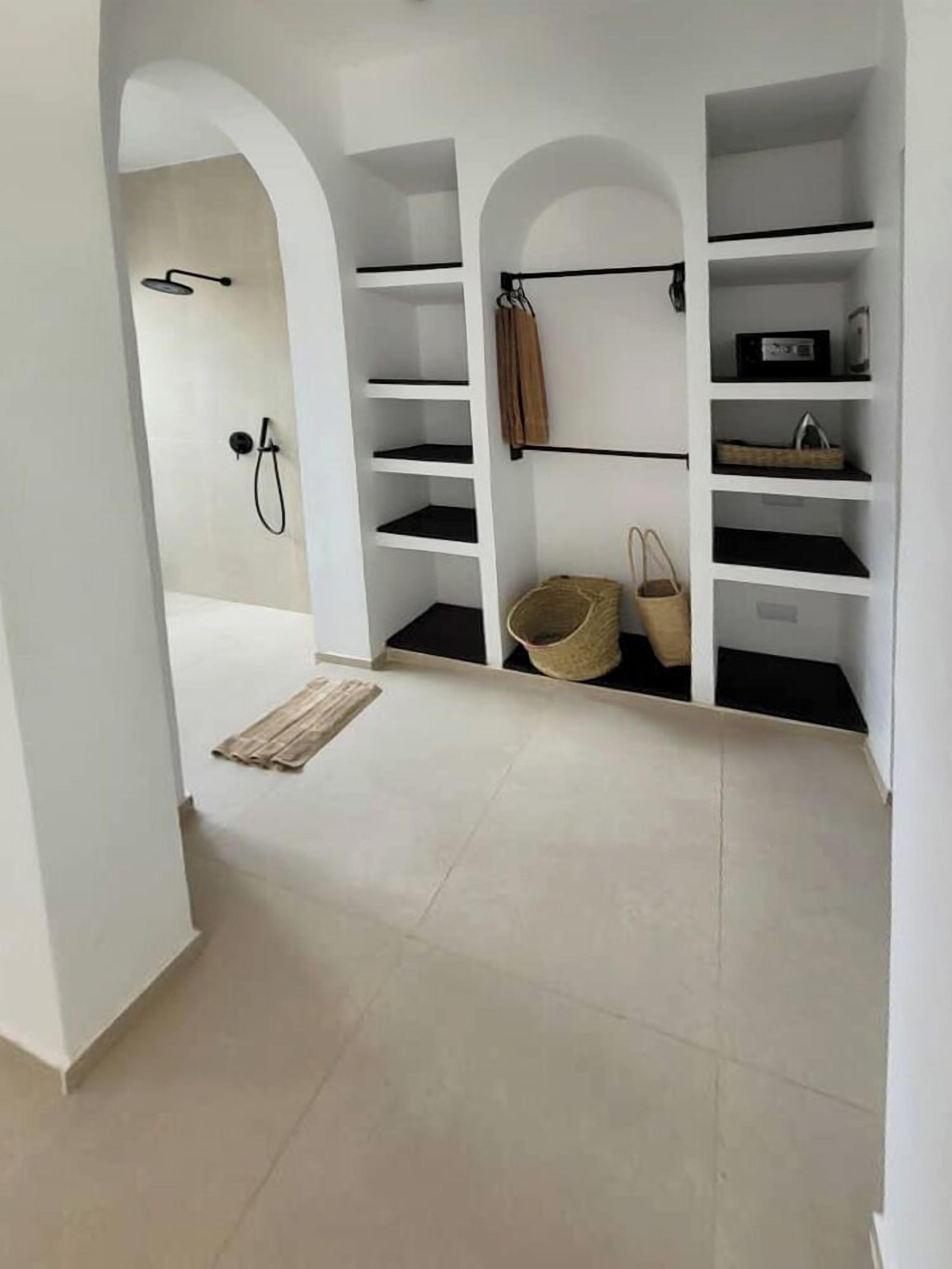 A walk-in closet with white shelving, a hanging rack, and a shower area.