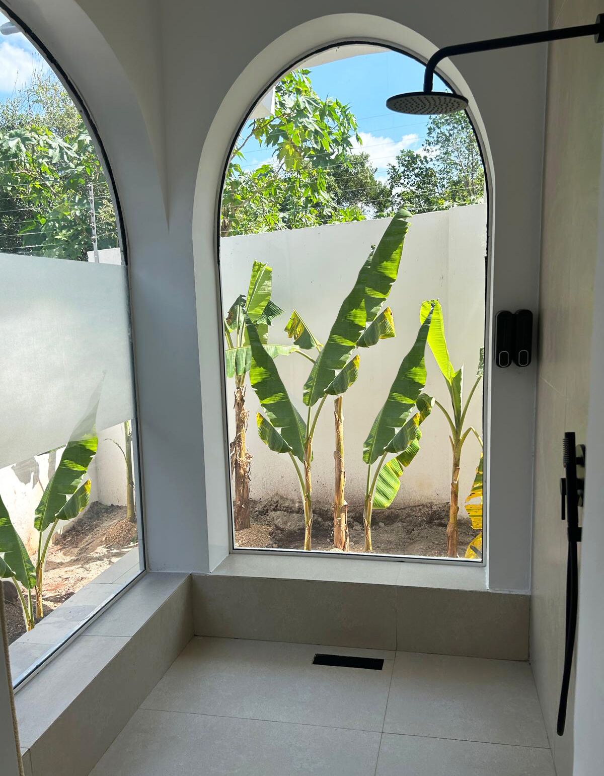 A bathroom with a large arched window, a showerhead, and a tiled floor.