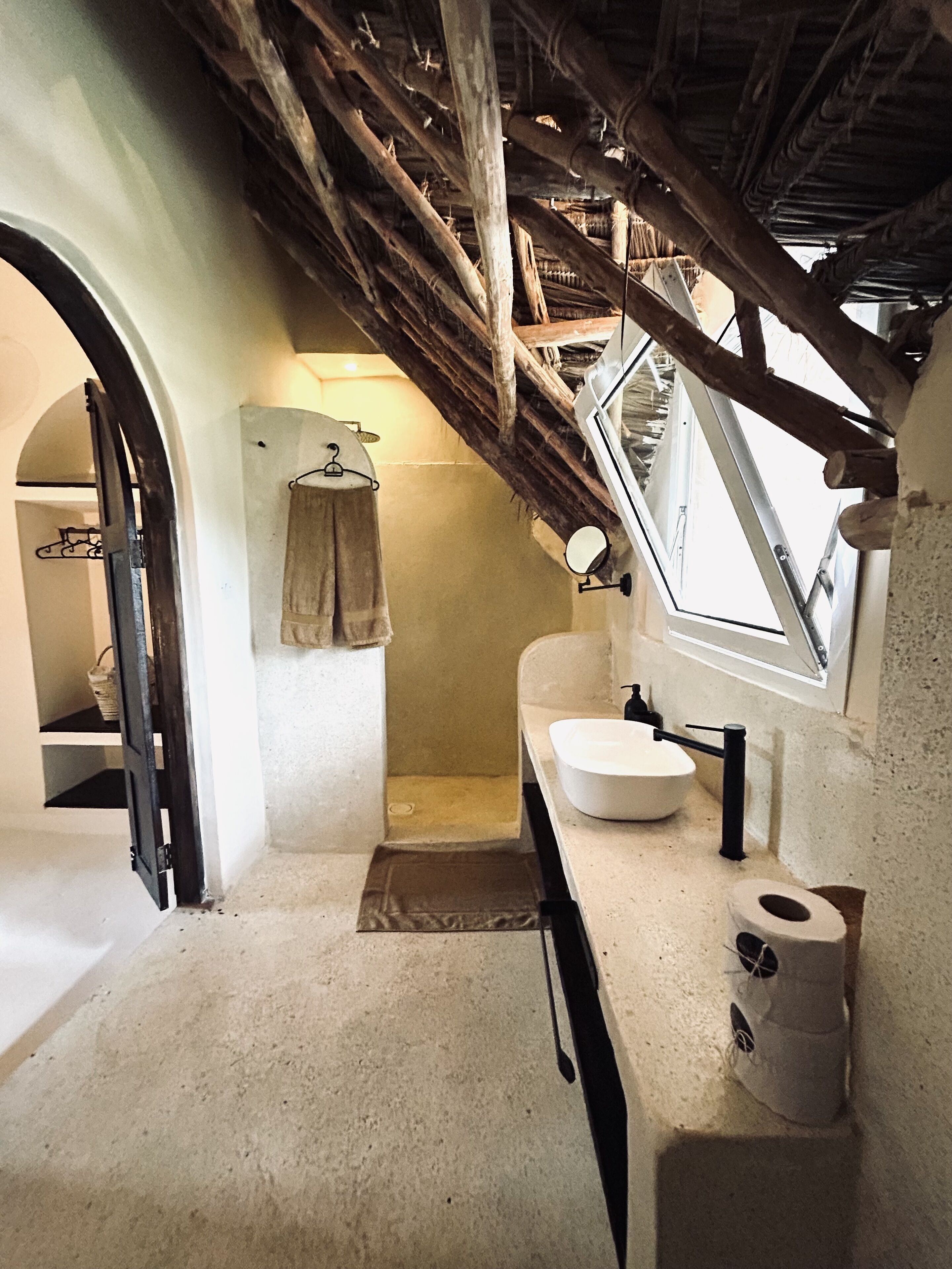 A rustic bathroom with a wooden ceiling, a white sink, a towel hanging on a rack, and a window above the sink.