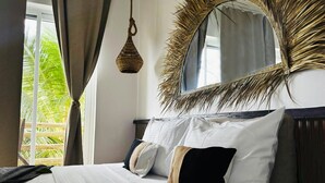 A bedroom with a bed, pillows, a hanging light, a mirror with a decorative frame, and a view of palm trees outside. - Kuwa Zanzibar (Kiwengwa)