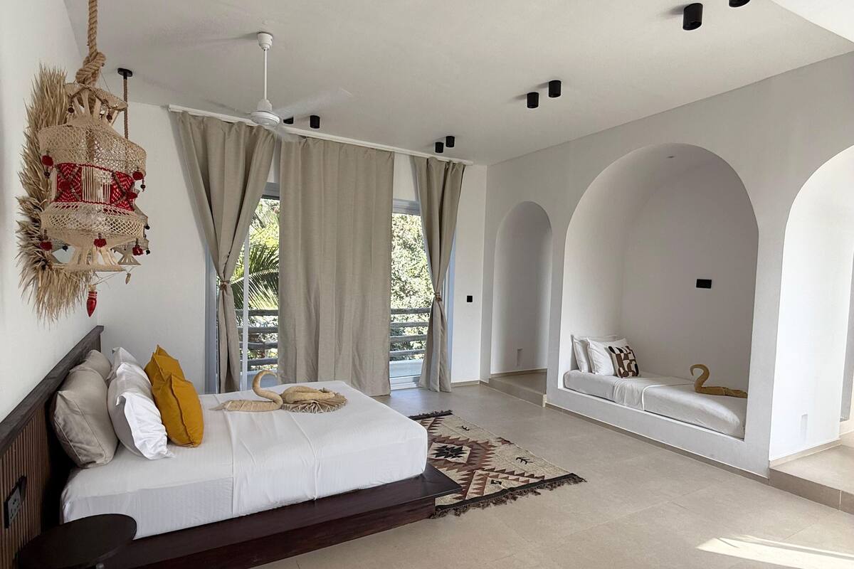 A spacious bedroom with a large bed, a sofa bed, and a hanging light fixture.