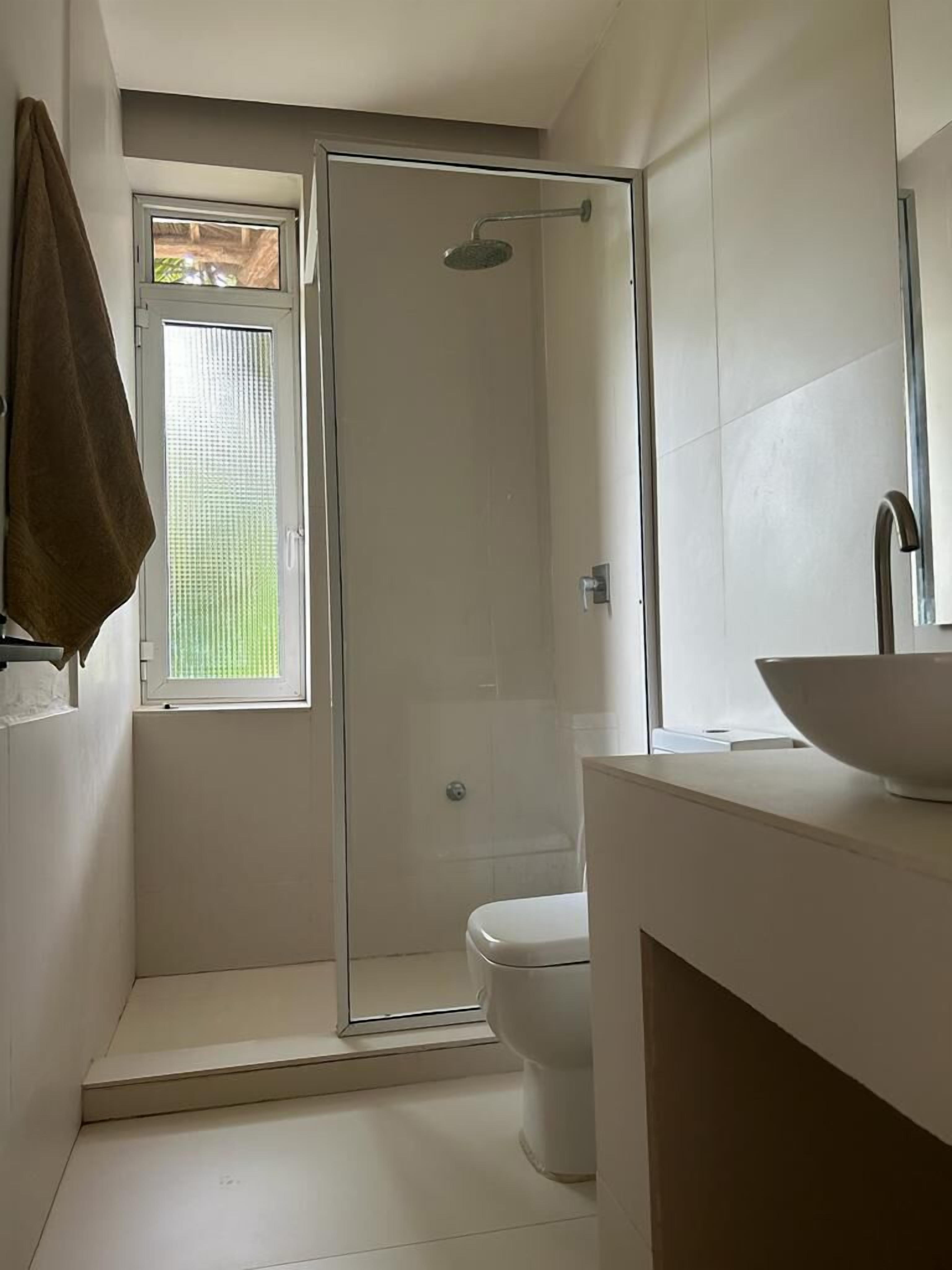 Een moderne badkamer met een douchecabine van glas, een wit toilet en een groot wit wastafel.