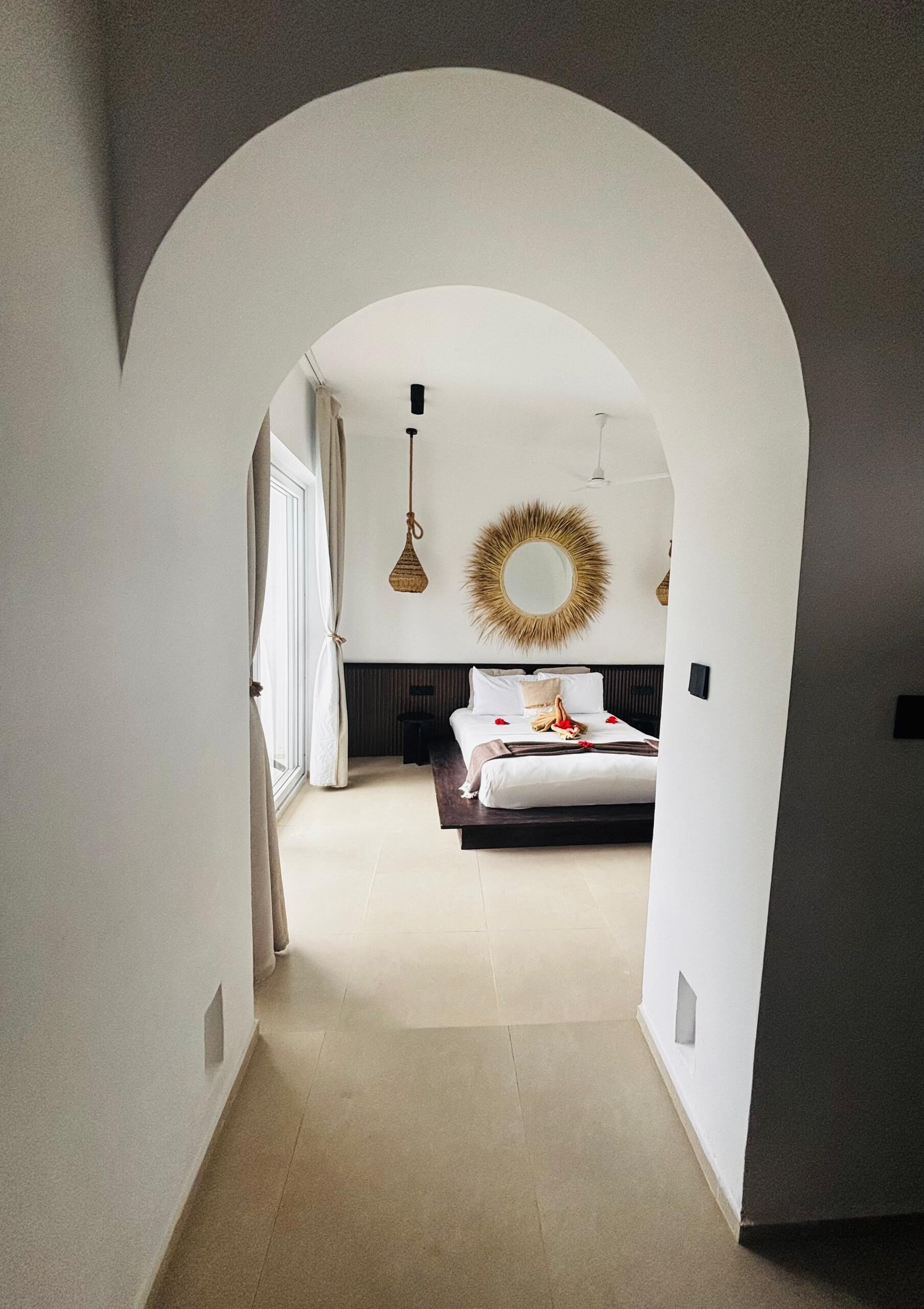 A bedroom with a bed, a mirror, and a hanging light fixture.
