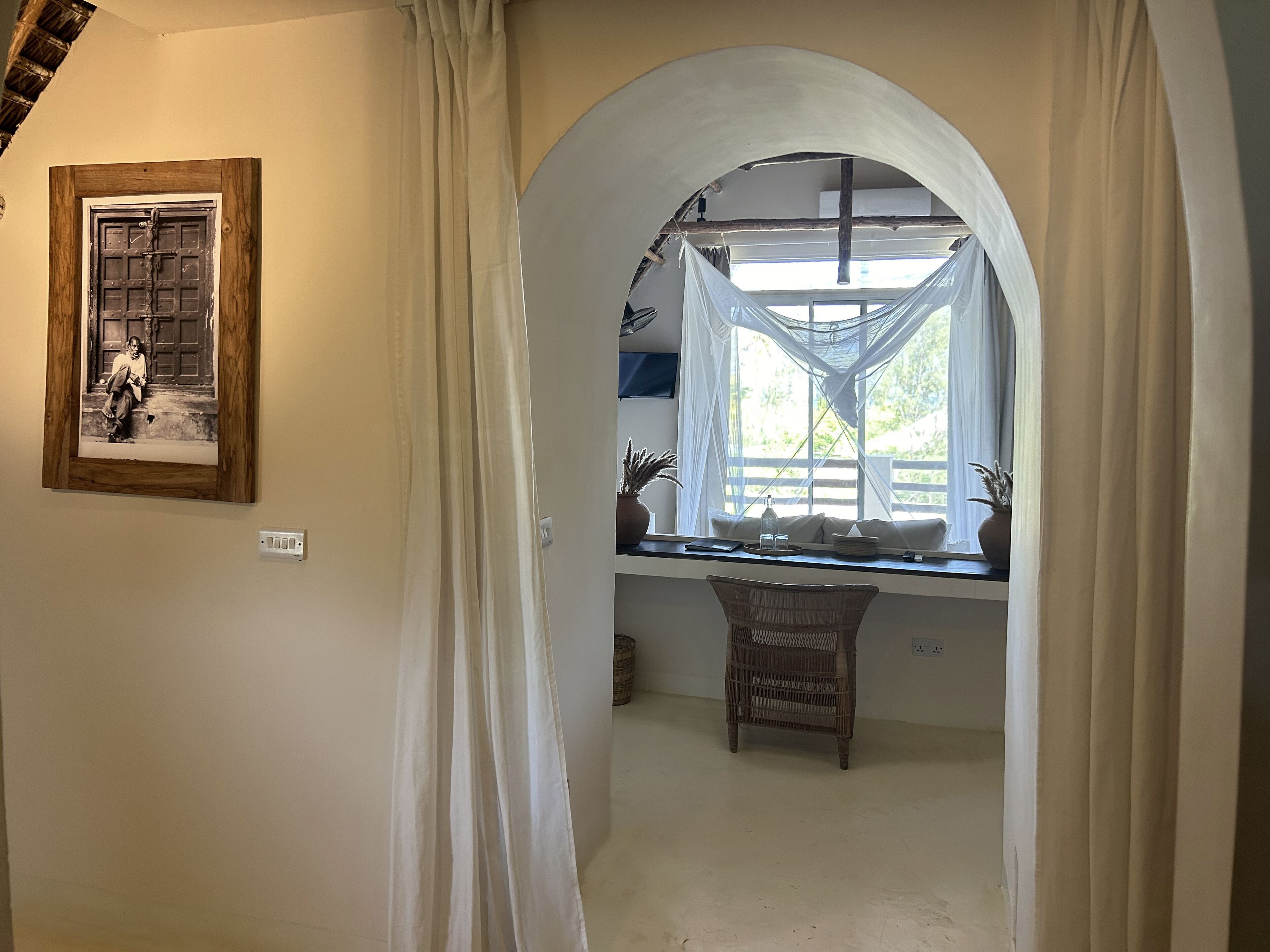 Ein Zimmer mit einem großen Bogenfenster, einem gerahmten Bild an der Wand und einem Korbstuhl in der Nähe des Fensters.