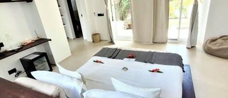 A modern hotel room with a large bed, a desk, and a view of greenery outside.