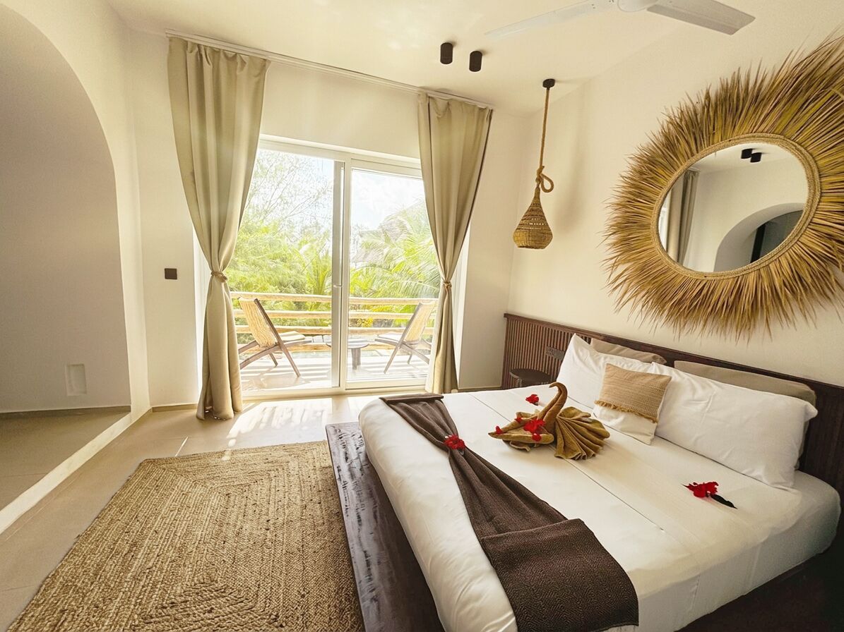 Een slaapkamer met een groot bed, een ronde spiegel en uitzicht op een balkon.